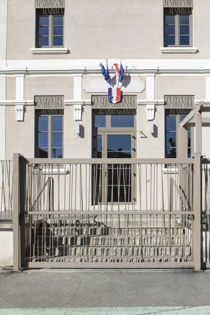 Entrée de l’école avec drapeaux et grille – école primaire d’Assieu (Isère), AEA Architecte Constructeur