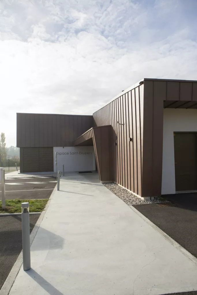 Allée d’accès au bâtiment en bardage métallique bronze – Espace Saint-Exupéry, Saint-Romain-d’Ay (Ardèche), AEA Architecte Constructeur
