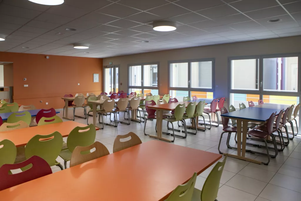 Salle de restauration lumineuse aux murs orange – restaurant scolaire de Grenay (Isère), AEA Architecte Constructeur